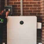 Technicus inspecteert het bedieningspaneel van een zonne-energiesysteem op een bakstenen muur.