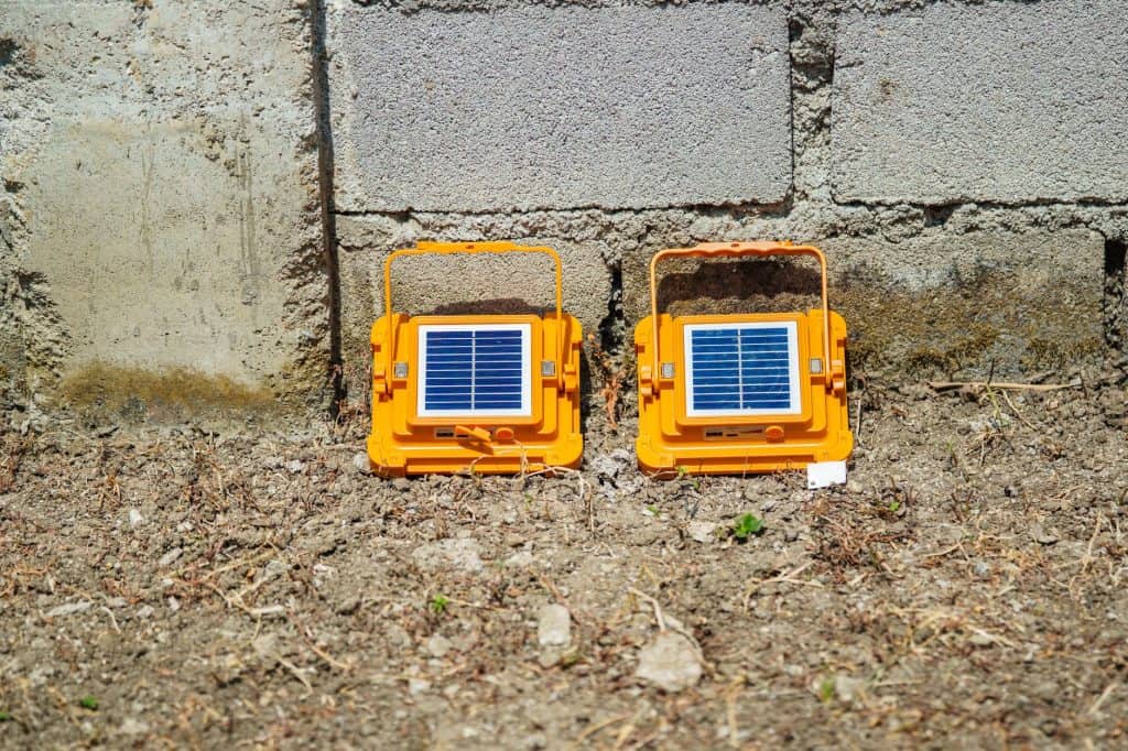 Solar-powered garden lights with solar panels on a dirt ground near a concrete wall.