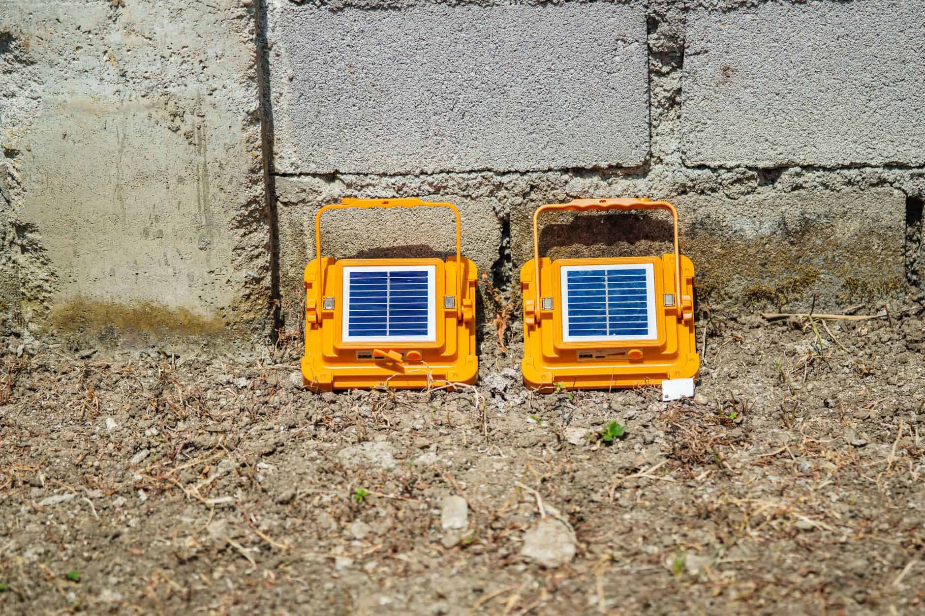 Solar-powered garden lights with solar panels on a dirt ground near a concrete wall.