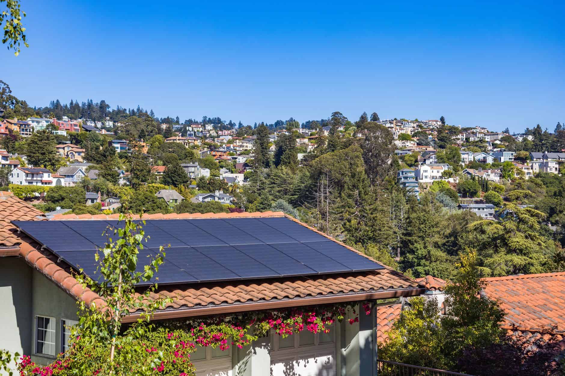 Solar panels installed on a house roof in a hilly neighborhood.