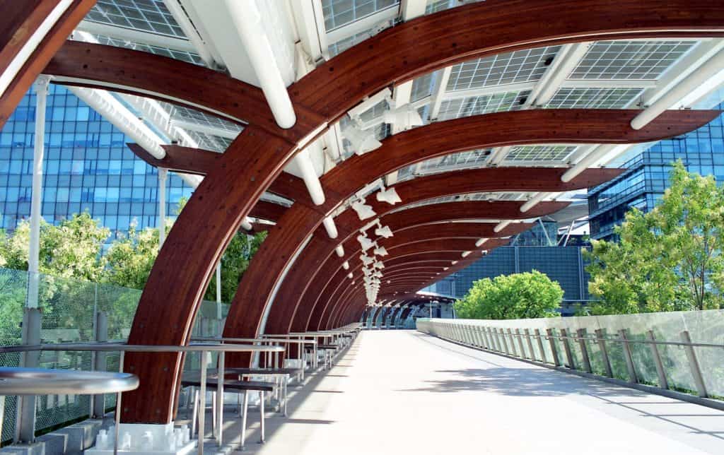 Modern urban walkway with wooden and glass canopy in a cityscape.