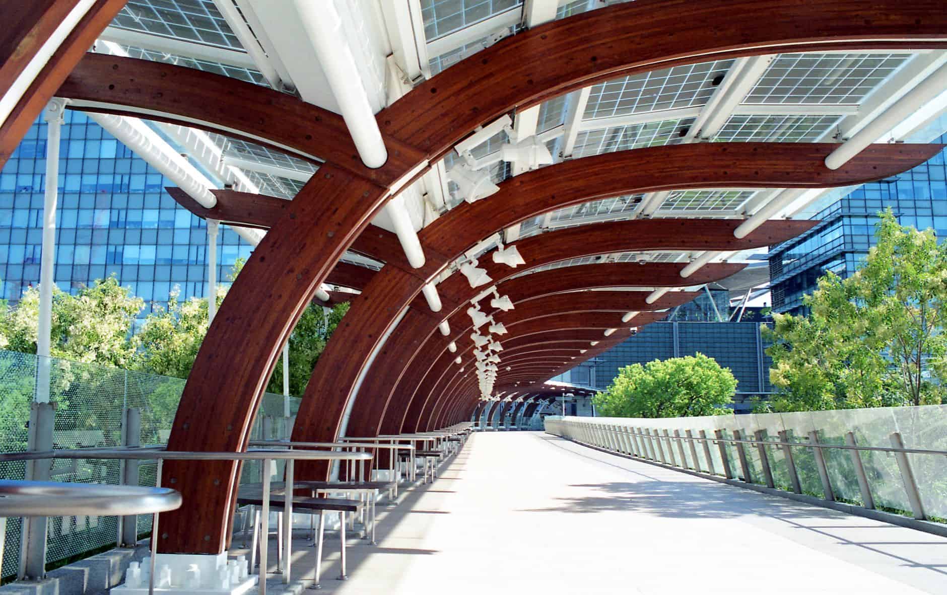Modern urban walkway with wooden and glass canopy in a cityscape.