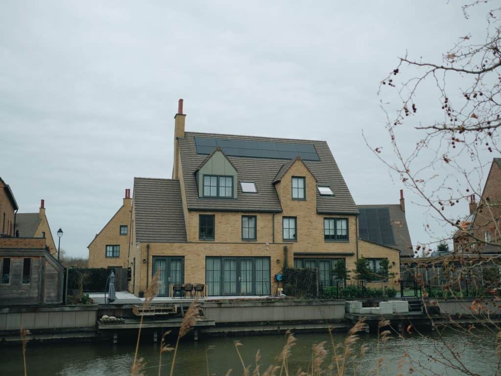 Modern house with solar panels on roof near water under cloudy sky.