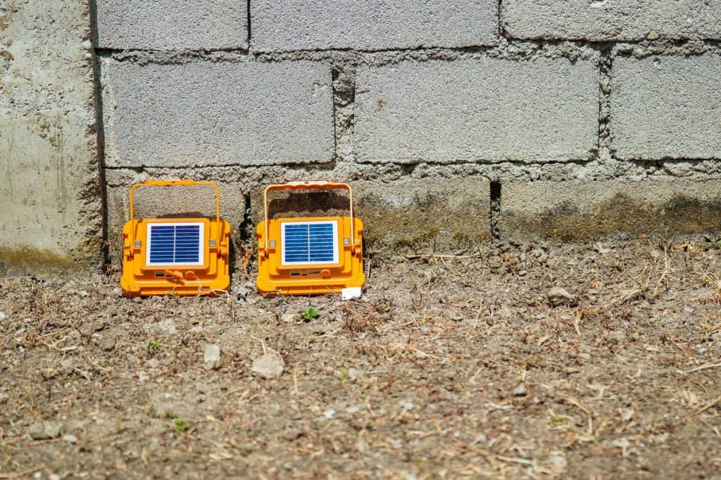Two small solar-powered devices placed on the ground near a brick wall.