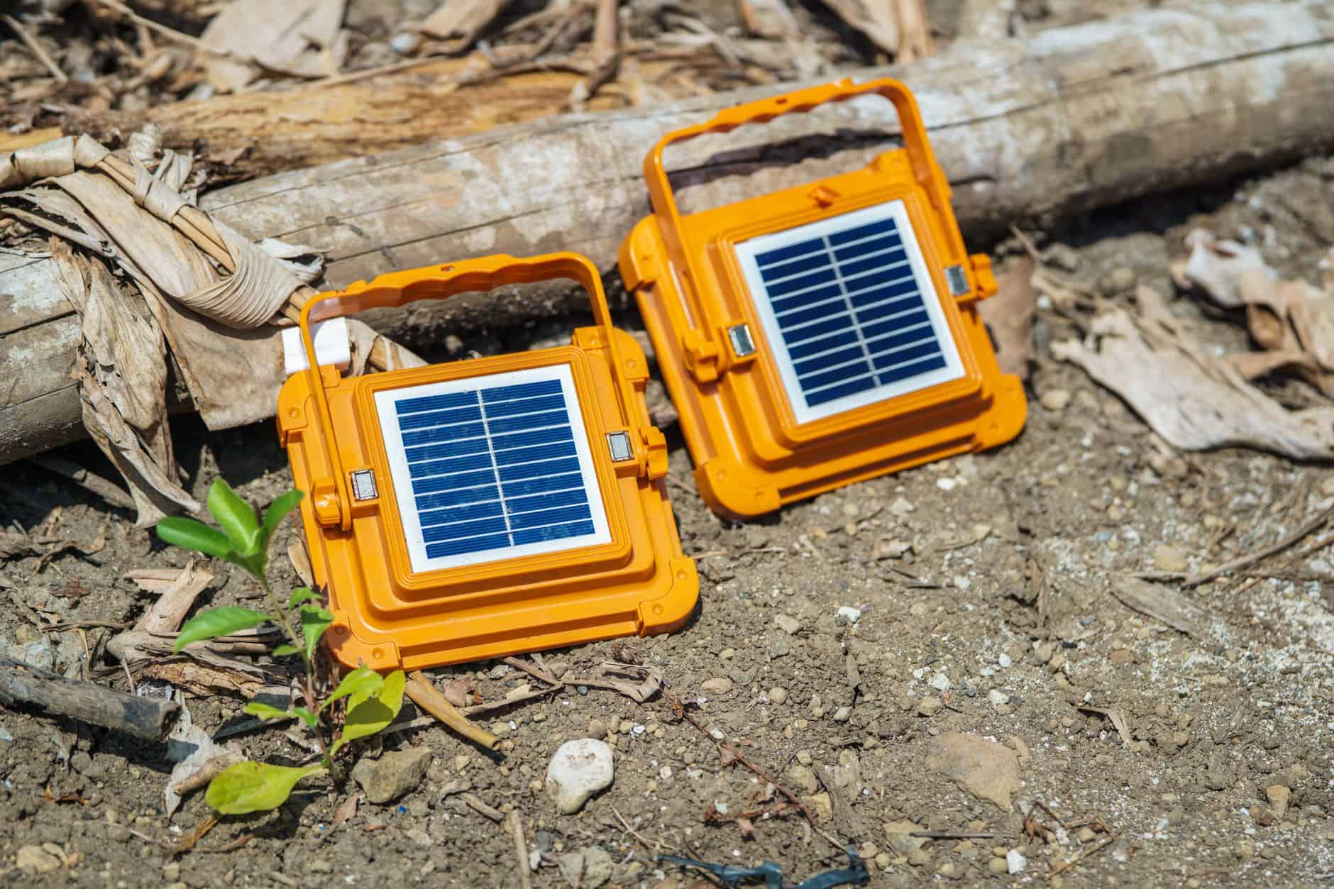 Portable solar-powered LED lights on outdoor ground with soil and wood debris.