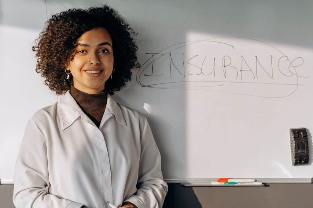 African American woman smiling in office setting with a whiteboard displaying 'Insurance'.