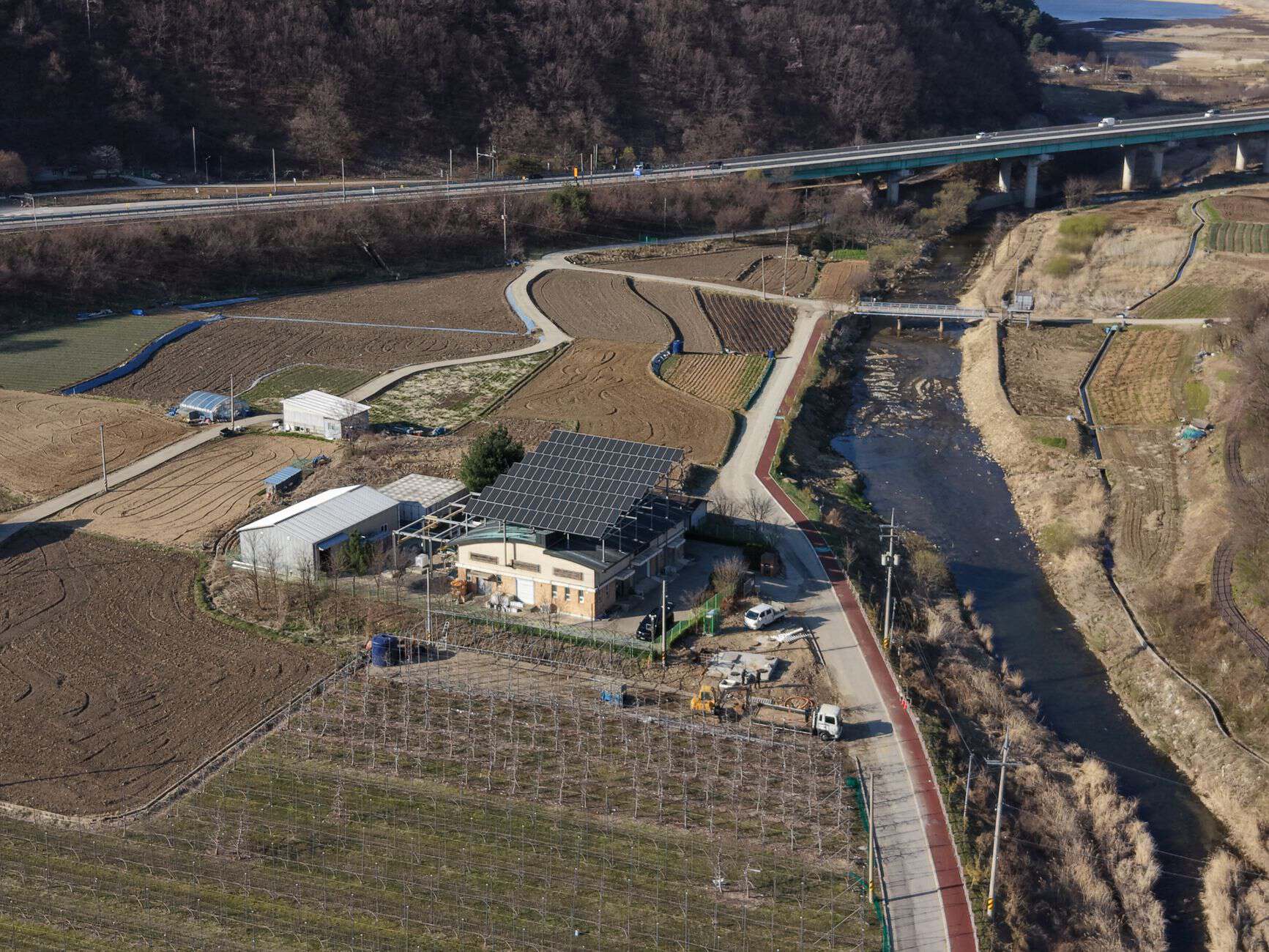 Aerial perspective of rural farmland featuring solar panels, fields, and a river.
