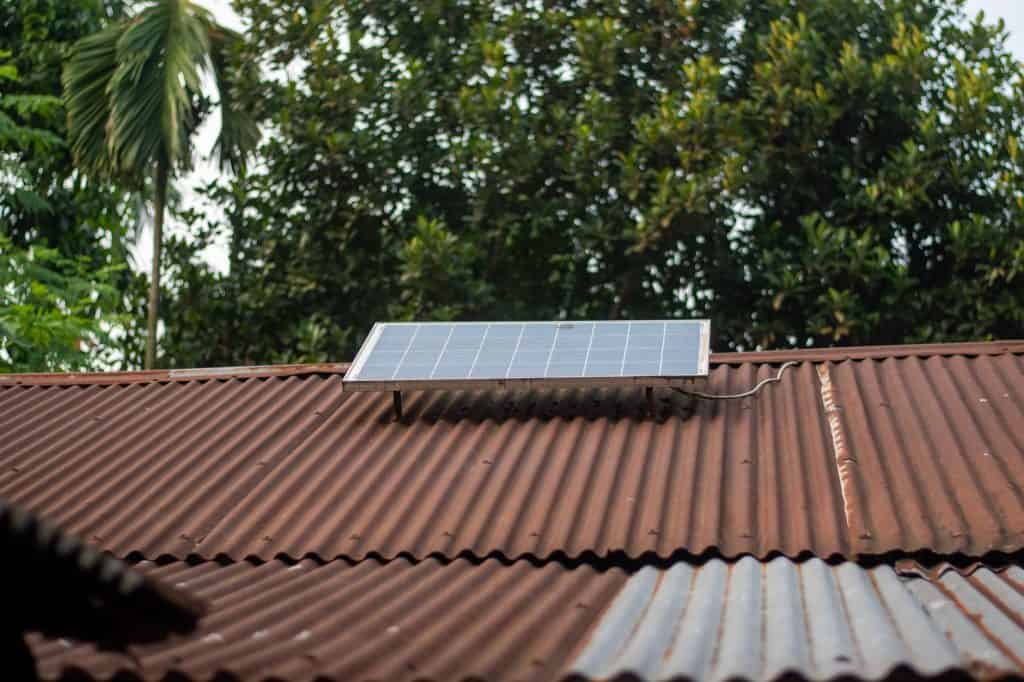 Solar panel installed on a rusted metal roof in a lush garden setting.