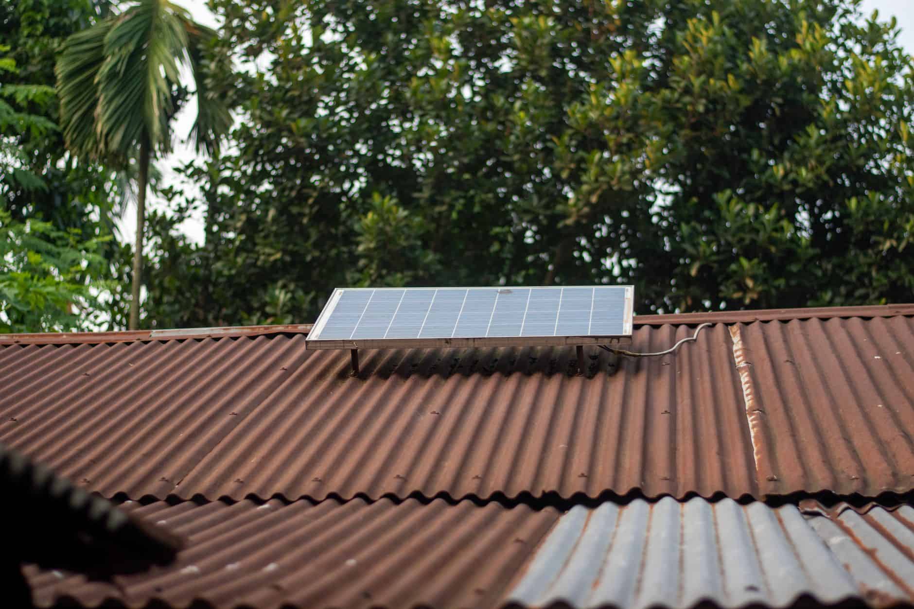 Solar panel installed on a rusted metal roof in a lush green environment.