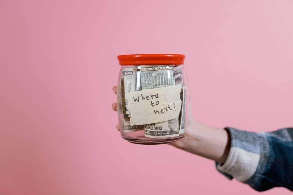 Een hand houdt een pot vast gevuld met geld en een briefje met de tekst 'Waar gaan we nu naartoe?'.