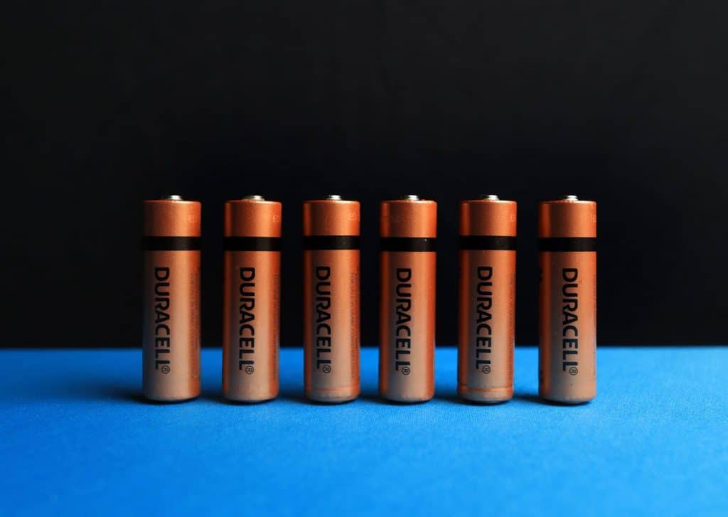Six DuraCell AA batteries lined up on a blue surface against a black background.