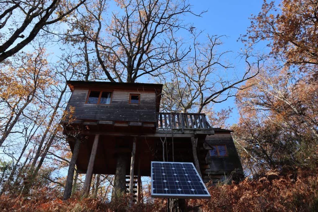 Rustic treehouse in vibrant autumn forest, featuring solar panel in Corrèze, France.