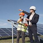 Young businessman in formal outfit and foreman in yellow vest looking away while discussing working process against sola