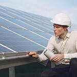 Focused young male employer in formal wear and hardhat working on solar panel station and checking details of modules