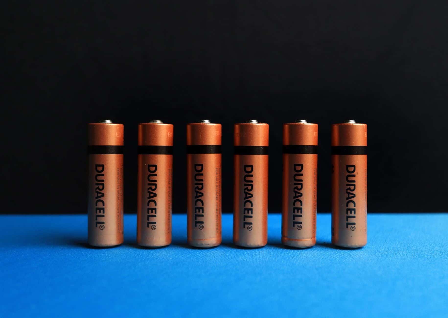 Six Duralock AA batteries lined up on a blue surface against a black background.